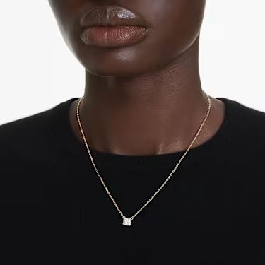 A model is wearing a black t shirt with a gold Swarovski Stilla pendant